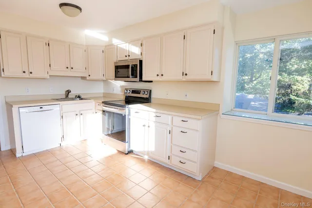 a kitchen with white cabinets appliances and a window