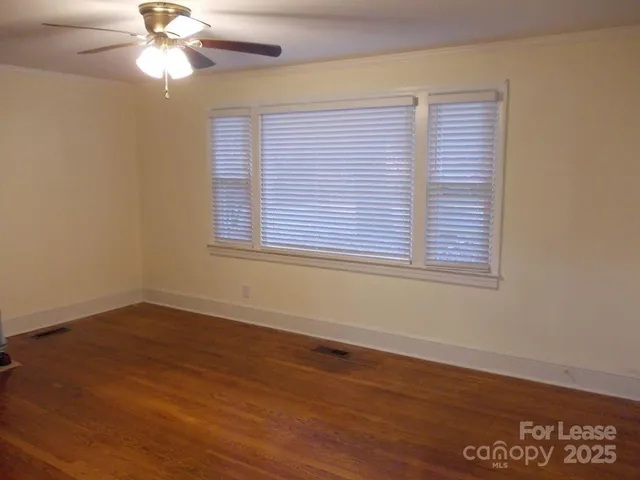 an empty room with wooden floor fan and windows