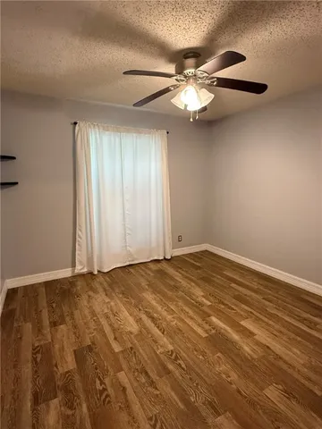 a view of an empty room with wooden floor and a ceiling fan
