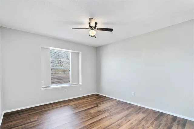 an empty room with wooden floor ceiling fan and windows