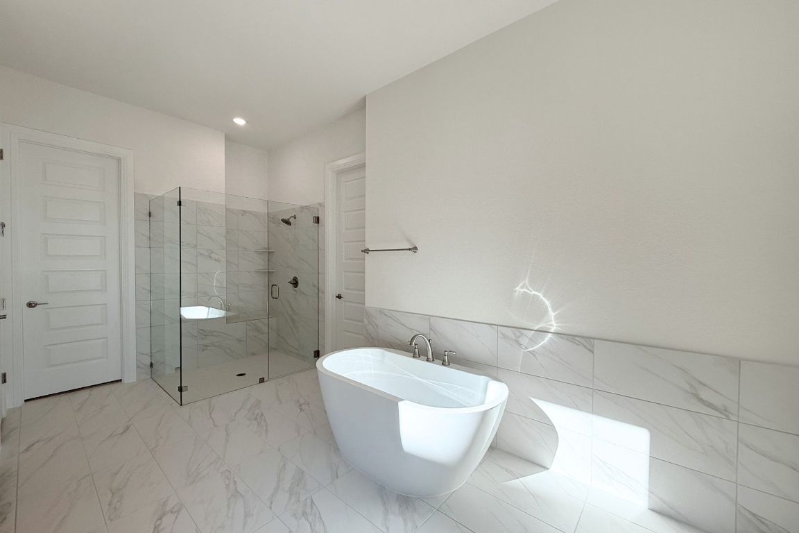 20301 Dustin Lane Pflugerville, TX 78660 - Photo 11 of 30 Full bathroom featuring a soaking tub, light marble finish flooring, tile walls, a marble finish shower, and wainscoting