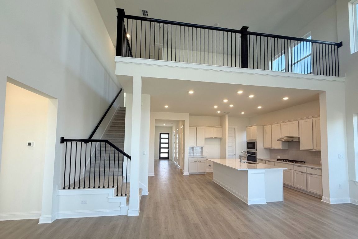 20301 Dustin Lane Pflugerville, TX 78660 - Photo 3 of 30 Kitchen with a towering ceiling, light wood finished floors, a kitchen island with sink, white cabinets, and recessed lighting