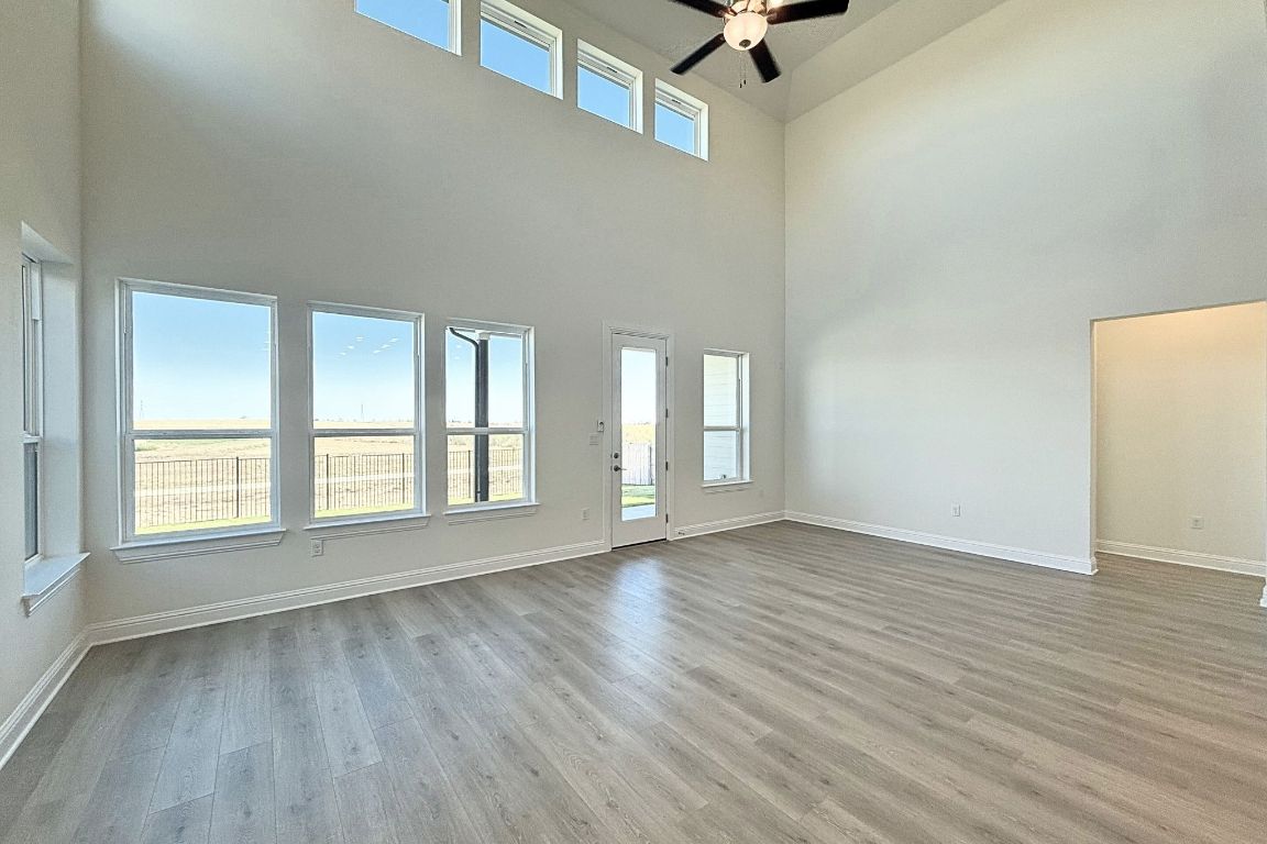 20301 Dustin Lane Pflugerville, TX 78660 - Photo 5 of 30 Unfurnished living room featuring light wood-style floors, healthy amount of natural light, a ceiling fan, and a high ceiling