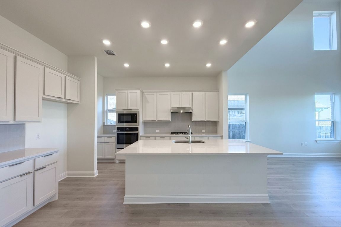 20301 Dustin Lane Pflugerville, TX 78660 - Photo 6 of 30 Kitchen featuring white cabinets, recessed lighting, stainless steel oven, a center island with sink, and light stone counters
