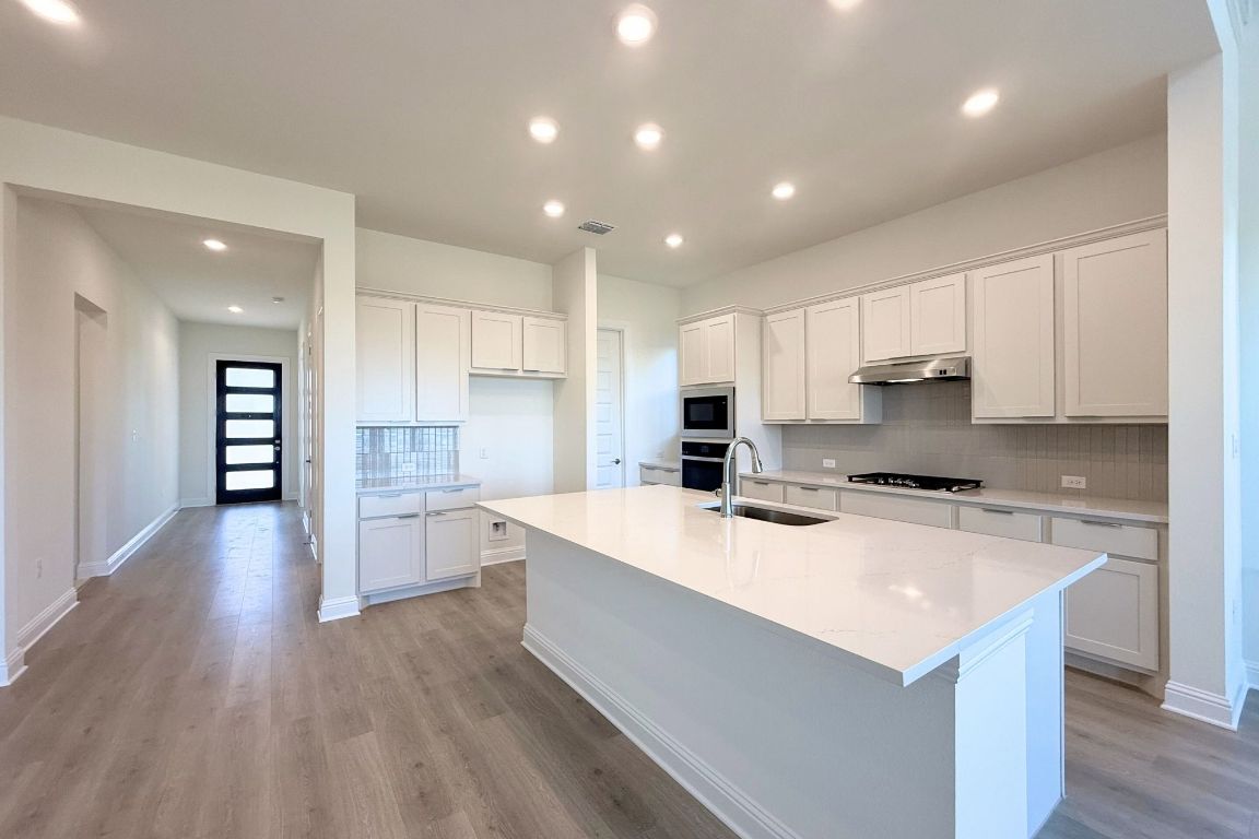 20301 Dustin Lane Pflugerville, TX 78660 - Photo 7 of 30 Kitchen with decorative backsplash, white cabinets, recessed lighting, a kitchen island with sink, and light stone countertops