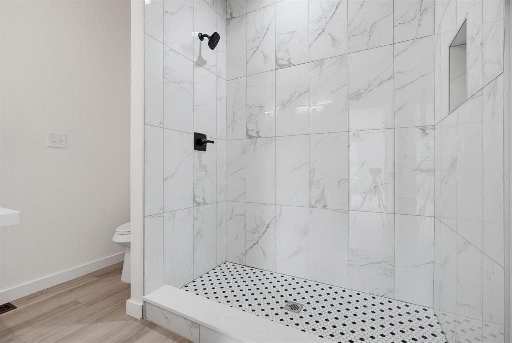 510 South O Connor Road Irving, TX 75060 - Photo 15 of 22 Shower enclosure featuring large format marble-look tile walls, a hexagonal mosaic tile floor, matte black shower fixtures, and a recessed niche