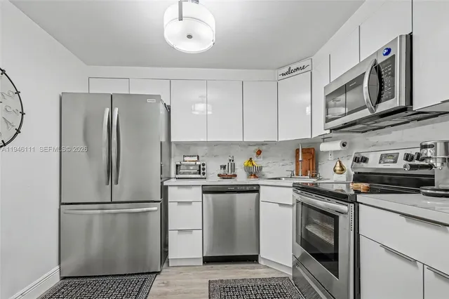 a kitchen with stainless steel appliances granite countertop a refrigerator a stove a sink and white cabinets