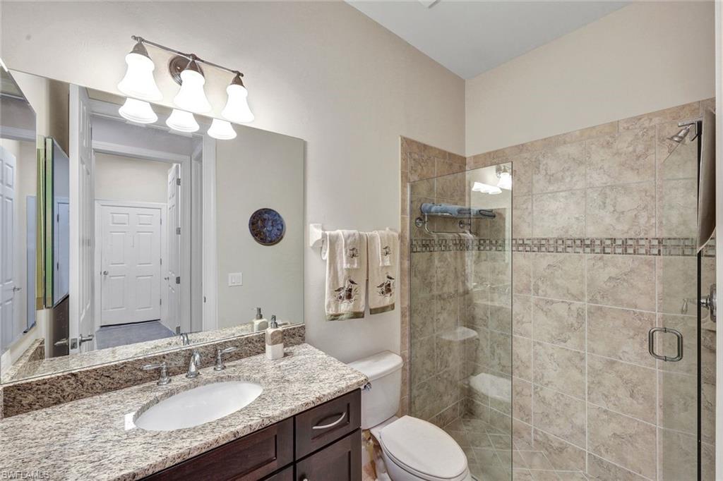 9111 Graphite Circle Naples, FL 34120 - Photo 17 of 33 a bathroom with a granite countertop sink toilet a mirror a vanity and shower