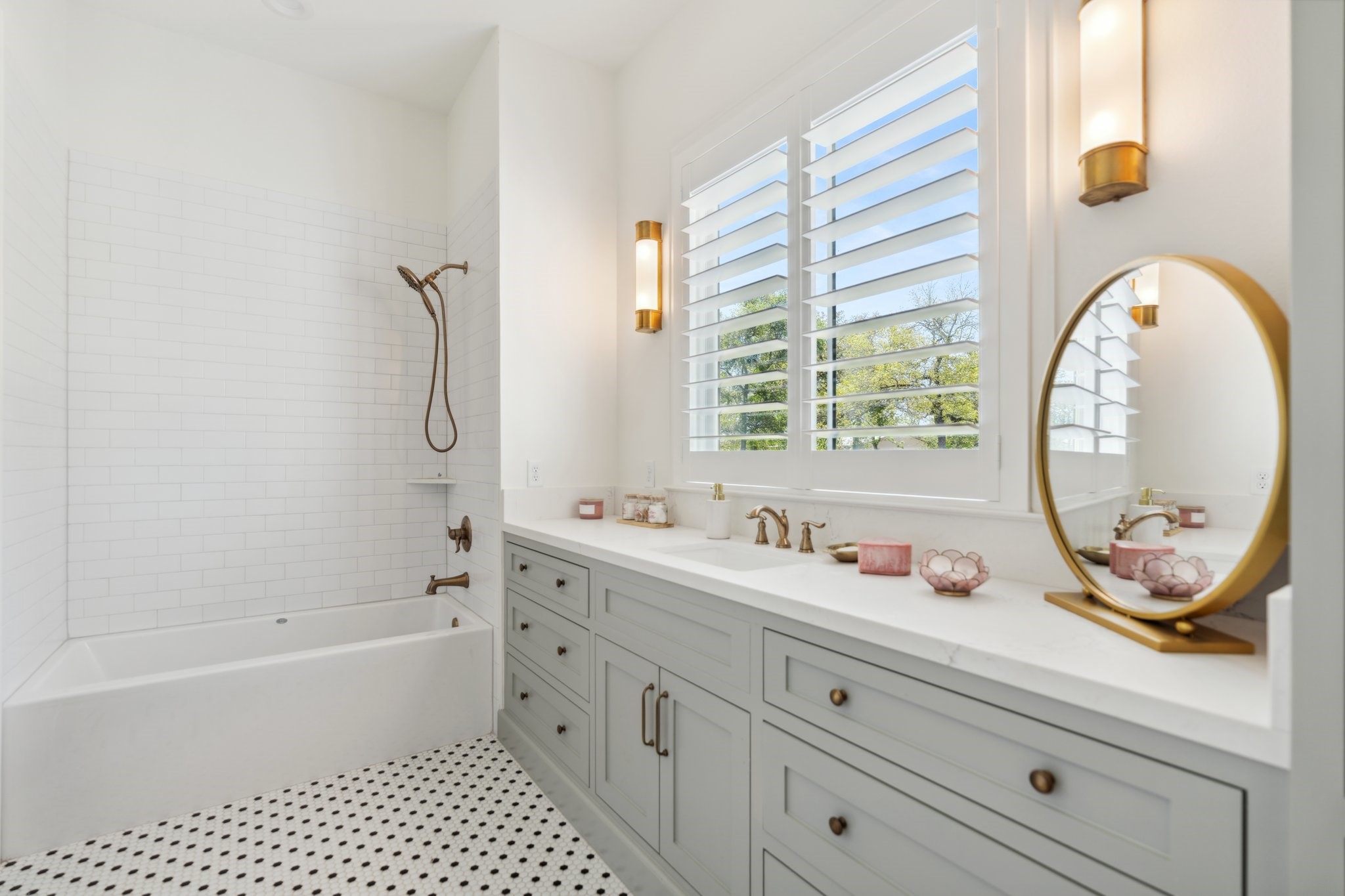 4052 Kuykendall Road Bellville, TX 77418 - Photo 19 of 40 This bathroom features a bright, elegant design with a white-tiled shower, a sleek vanity with gold fixtures, and ample natural light from the window with plantation shutters. The patterned floor adds a touch of sophistication.