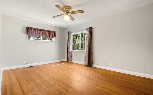 an empty room with wooden floor ceiling fan and windows