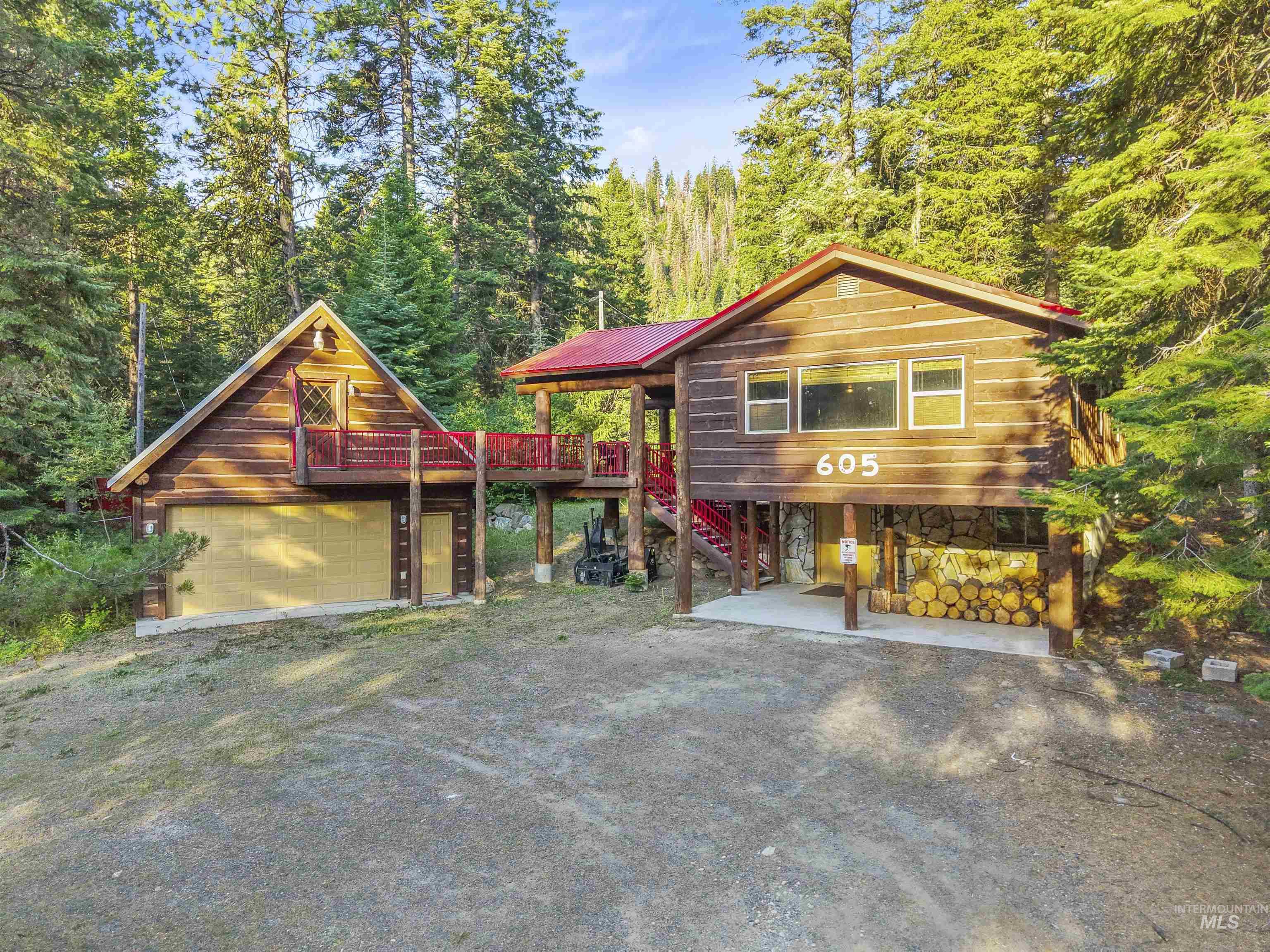 View of front facade with stairs, a wooden deck, a metal roof, a wooded view, and stone siding