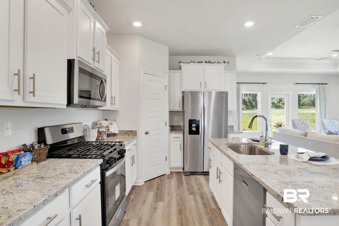 13822 Antler Hl Road Daphne, AL 36527 - Photo 30 of 39 Kitchen featuring stainless steel appliances, light stone counters, sink, white cabinetry, and light hardwood / wood-style flooring