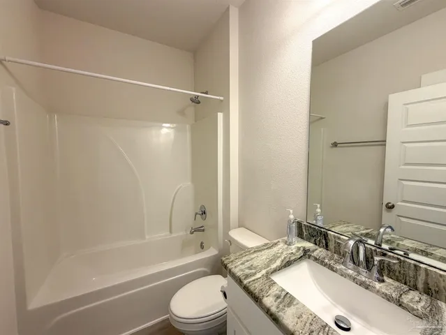 a bathroom with a granite countertop bathtub shower sink vanity mirror and toilet