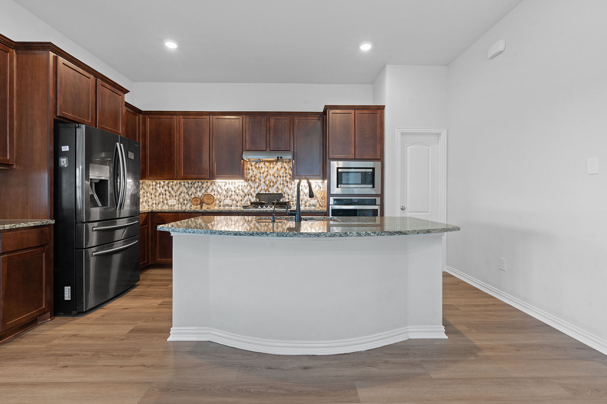 213 Treasure Trove Path Kyle, TX 78640 - Photo 4 of 29 Kitchen featuring dark stone countertops, stainless steel appliances, an island with sink, light wood finished floors, and recessed lighting