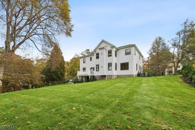 a view of a white house in front of a big yard with large trees