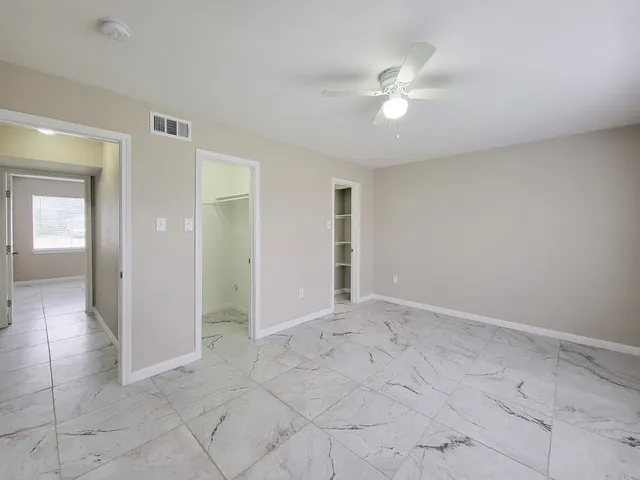 an empty room with fan and way to kitchen