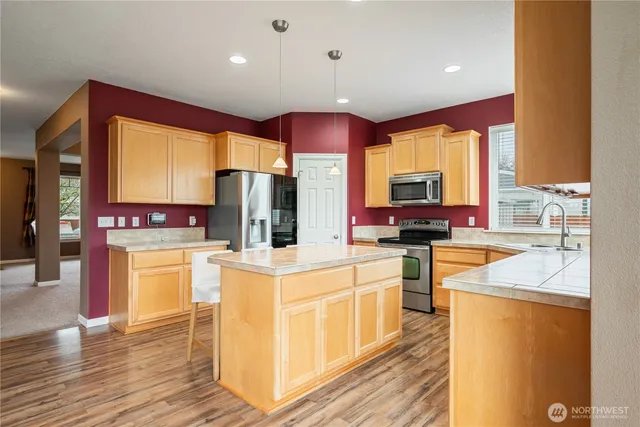 a kitchen with stainless steel appliances kitchen island granite countertop a stove a sink dishwasher and a refrigerator with wooden floor