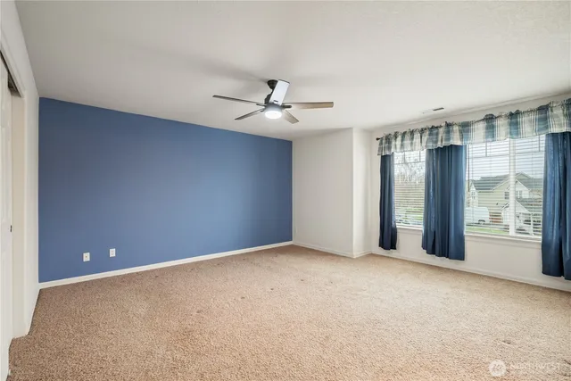 an empty room with chandelier fan and windows
