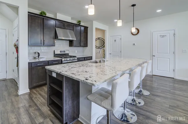a kitchen with granite countertop a stove a kitchen island a sink dishwasher a dining table and chairs with wooden floor