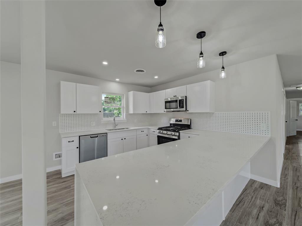 309 East Obuch Street Valley View, TX 76272 - Photo 10 of 24 Kitchen featuring new appliances with stainless steel finishes, a peninsula, decorative backsplash, white cabinets, and light stone countertops
