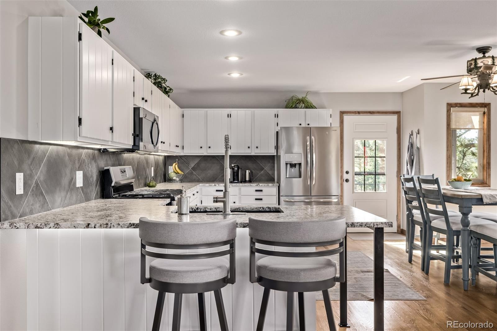 13950 Pine Valley Road Pine, CO 80470 - Photo 9 of 49 a kitchen with stainless steel appliances granite countertop a stove top oven a refrigerator a sink and a dining table with white cabinets