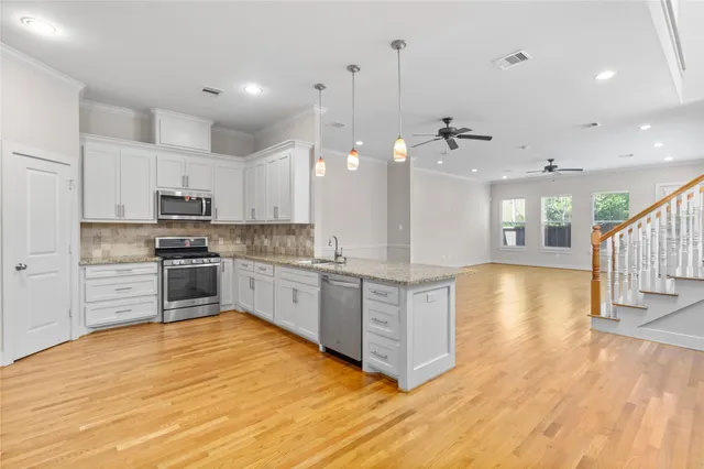 a large kitchen with stainless steel appliances granite countertop a large center island a stove a refrigerator white cabinets and wooden floor