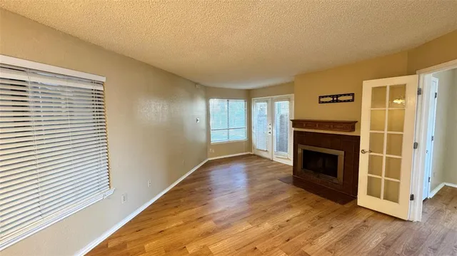 a view of an empty room with wooden floor fireplace and a window