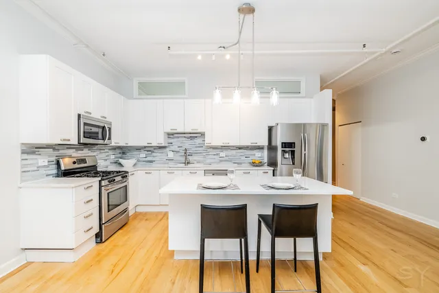 a kitchen with stainless steel appliances kitchen island granite countertop a table chairs and a refrigerator