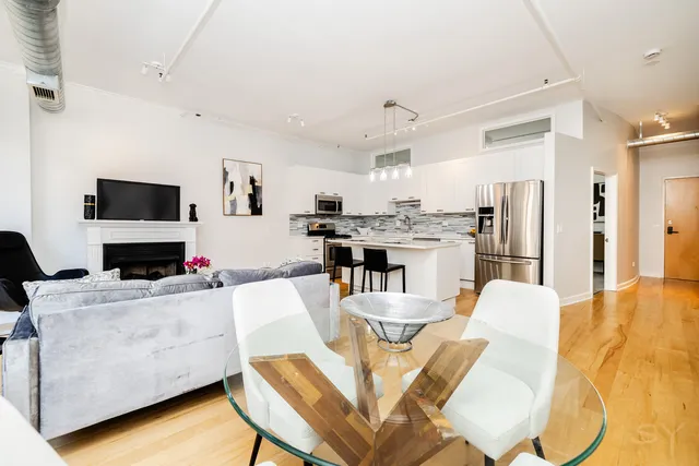 a living room with stainless steel appliances furniture a fireplace and a kitchen view