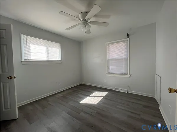 an empty room with wooden floor chandelier fan and windows