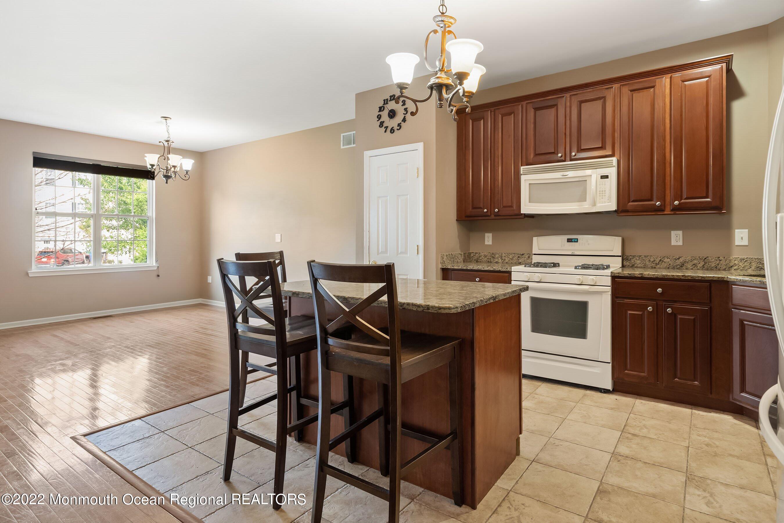 107 Bryce Lane, Unit 2004 Manahawkin, NJ 08050 - Photo 7 of 39 a kitchen with stainless steel appliances granite countertop a stove a sink dishwasher a dining table and chairs with wooden floor