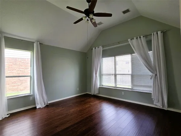 an empty room with wooden floor fan and windows