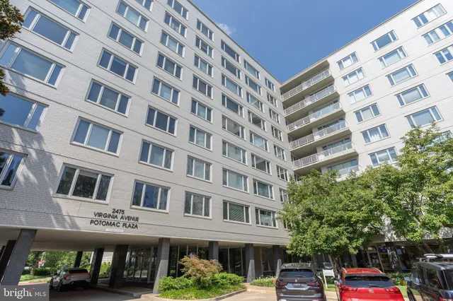 a front view of a building with lot of cars and trees