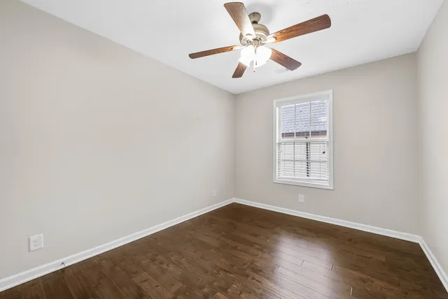an empty room with wooden floor ceiling fan and windows