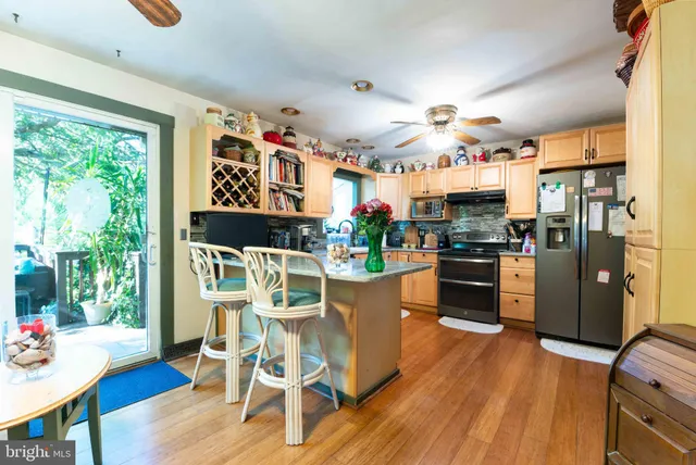 a kitchen with stainless steel appliances kitchen island granite countertop a refrigerator a stove top oven a dining table and chairs with wooden floor