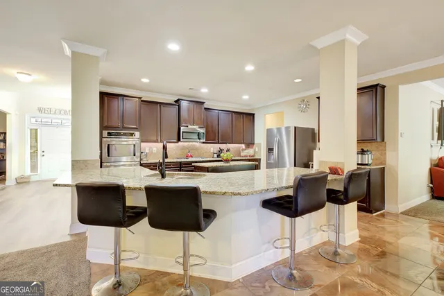 a kitchen with stainless steel appliances kitchen island granite countertop a dining table chairs and a refrigerator