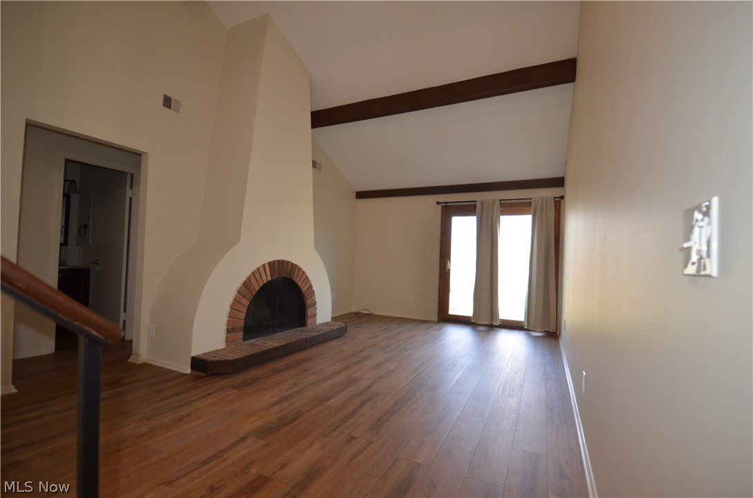 6933 West Fitzwater Road Brecksville, OH 44141 - Photo 3 of 18 Living room featuring vaulted ceiling, wood beam accents, new vinyl flooring, and a brick fireplace. Doors to the patio at the rear.