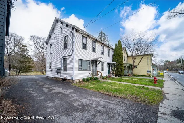 a view of a white house with a big yard and large tree