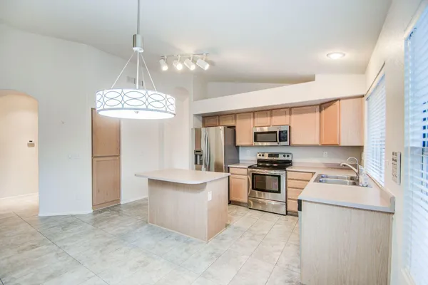 a kitchen with stainless steel appliances a stove top oven a sink dishwasher a refrigerator and a dining table with wooden floor