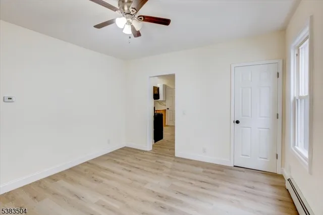 a view of an empty room with wooden floor and a ceiling fan
