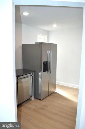 a view of a refrigerator in kitchen and an empty room in wooden floor