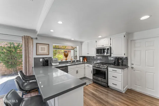 a kitchen with stainless steel appliances granite countertop a stove top oven a sink dishwasher and white cabinets with wooden floor