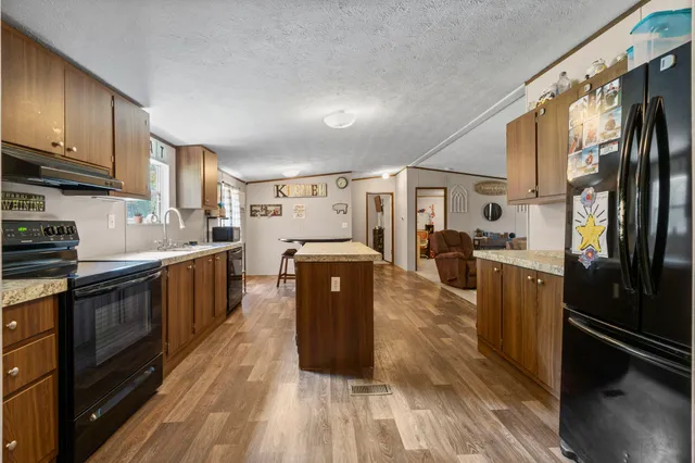 a kitchen with stainless steel appliances granite countertop a refrigerator a stove top oven a sink dishwasher and wooden cabinets with wooden floor