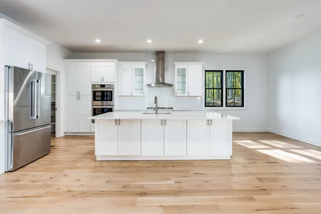 a view of kitchen with stainless steel appliances granite countertop a stove a sink a refrigerator and white cabinets with wooden floor