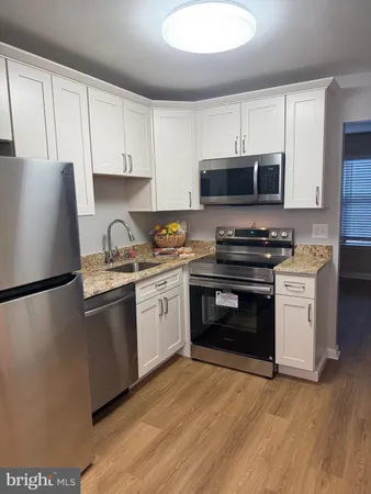 a kitchen with granite countertop a refrigerator stove and sink with wooden floor