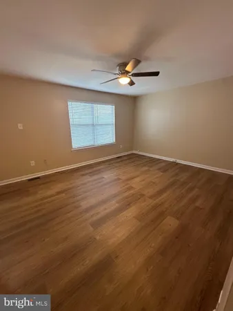 an empty room with wooden floor ceiling fan and windows