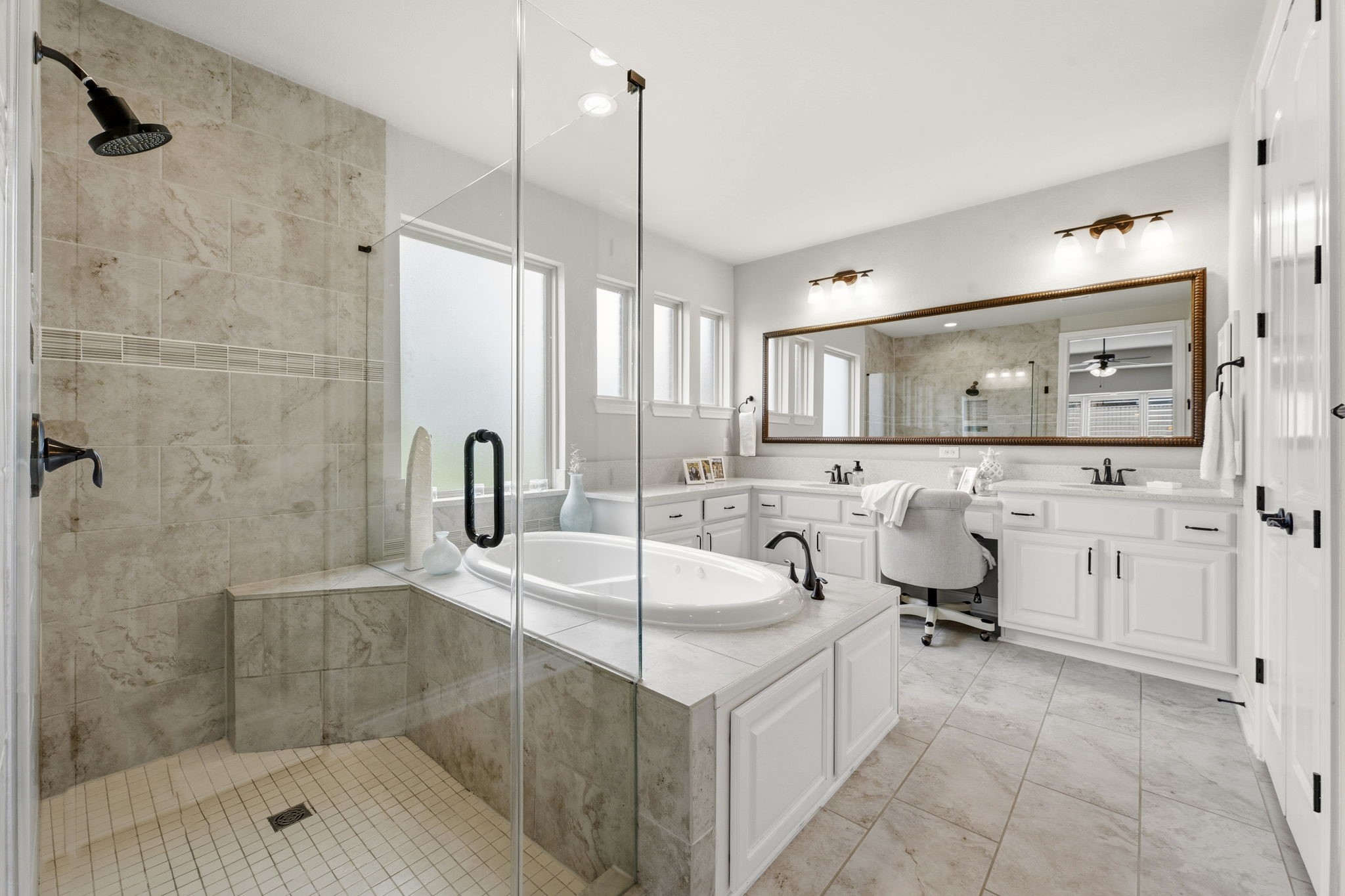 14012 Beartooth Bend Trail Conroe, TX 77384 - Photo 21 of 50 Truly a private retreat for both busy mornings and relaxing evenings, the en-suite bath is designed with comfort and elegance in mind. An elegant double-door entry opens to rectangular tile flooring, recessed lighting, dual vanities, a jetted tub, and a spacious walk-in shower. Four windows with textured glass provide abundant natural light while maintaining privacy. Additional features include a private commode and a generous walk-in closet.