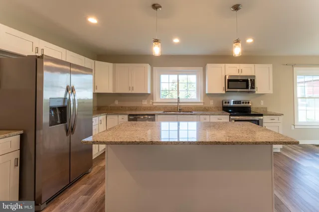 a view of an empty room and kitchen with hardwood floor