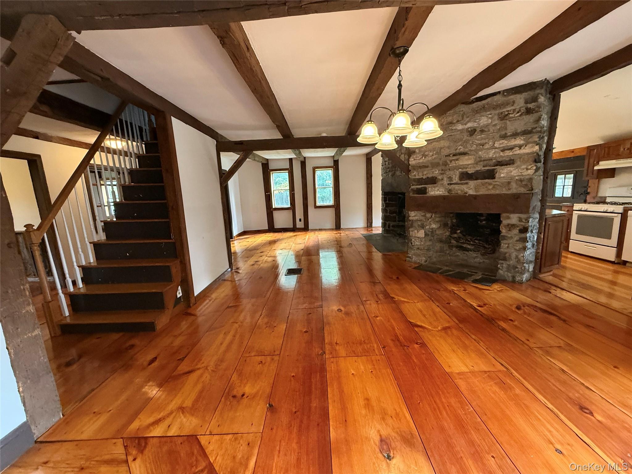 241 White Bridge Road Middletown, NY 10940 - Photo 14 of 29 Unfurnished living room with light wood finished floors, a stone fireplace, beamed ceiling, stairs, and a chandelier