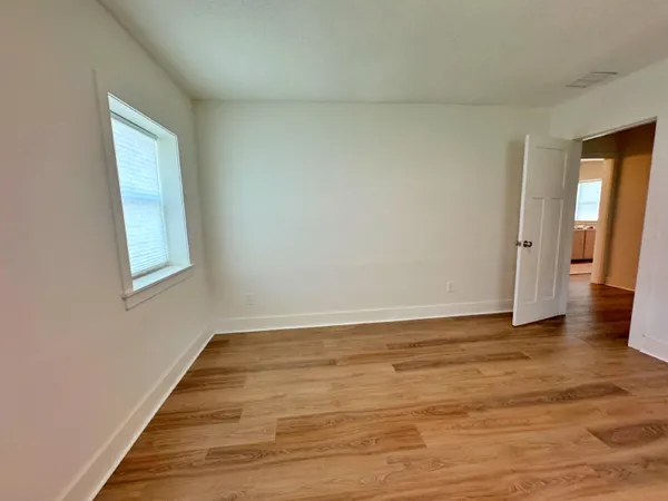 a view of an empty room with wooden floor and a window